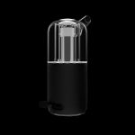 Sleek, cylindrical cannabis vaporizer with a clear glass chamber and textured black base, studio shot on black background.