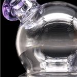 A clear glass dab rig with a purple-accented mouthpiece, showcasing swirling glass patterns.