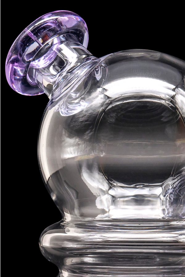 A clear glass dab rig with a purple-accented mouthpiece, showcasing swirling glass patterns.