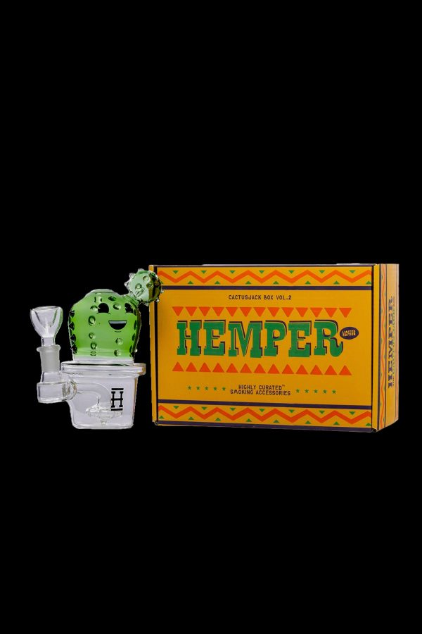 A vibrant green cactus-shaped water pipe stands beside a decorated box labeled "Hempter Cactus Jack Vol. 2" with text indicating “highly curated” smoking accessories.