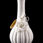 White ceramic bubbler with sculpted roses, reflecting on a black surface.