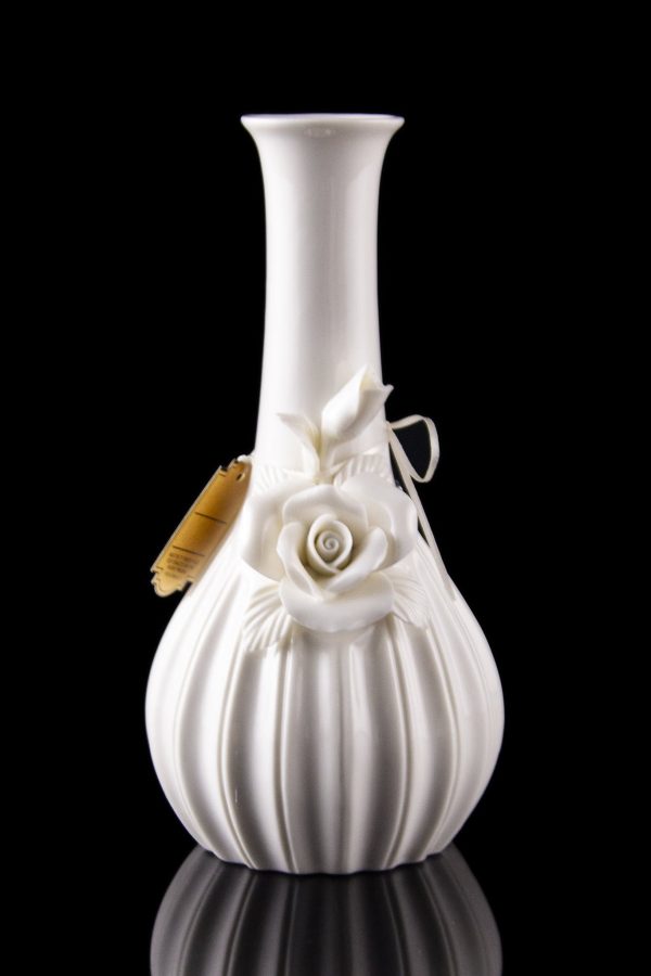 White ceramic bubbler with sculpted roses, reflecting on a black surface.
