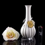 Elegant glass cannabis water pipe with a floral arrangement and lighter, reflected on a glossy black surface.