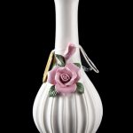 White ceramic bubbler with delicate pink rose embellishment, reflecting on a dark surface.