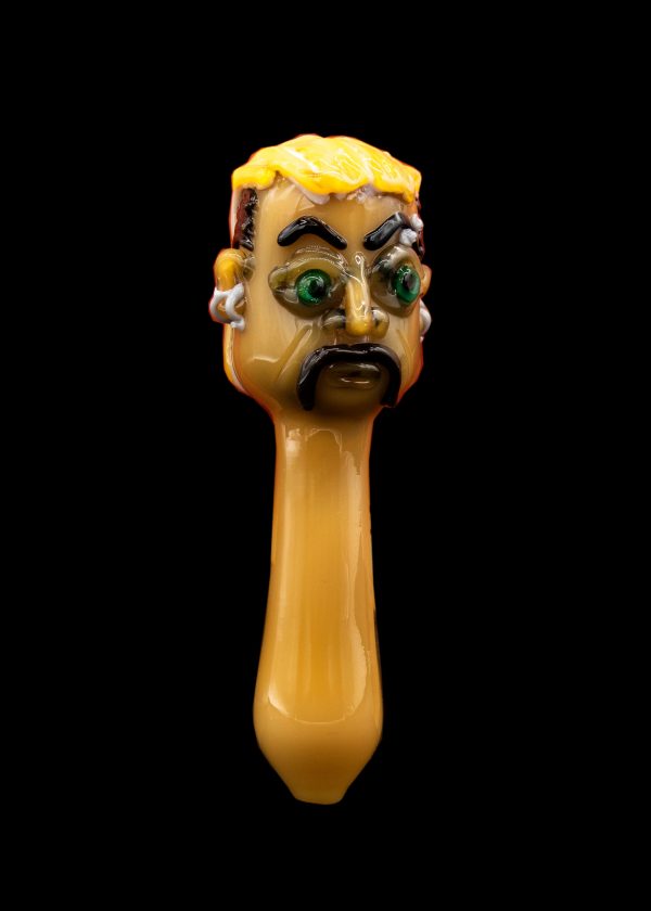 Hand-blown glass pipe shaped like a cartoonish face with green eyes, against a black background.