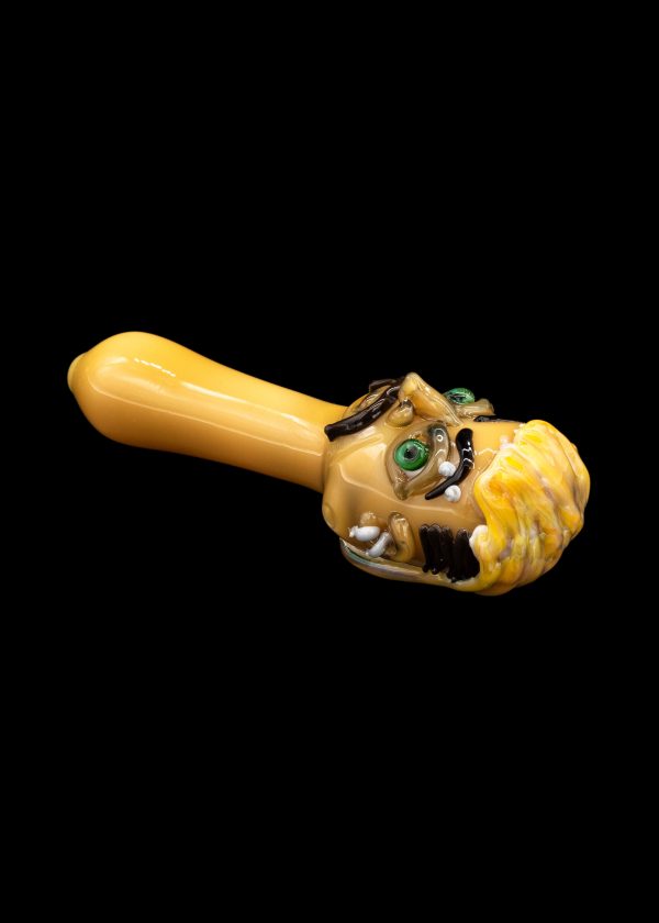 Hand-blown glass cannabis pipe sculpted as a monster head with exposed teeth and glowing green eyes.