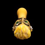 A vibrant, hand-blown glass cannabis water pipe shaped like a stylized monster head with intricate detailing and a yellow, textured body.