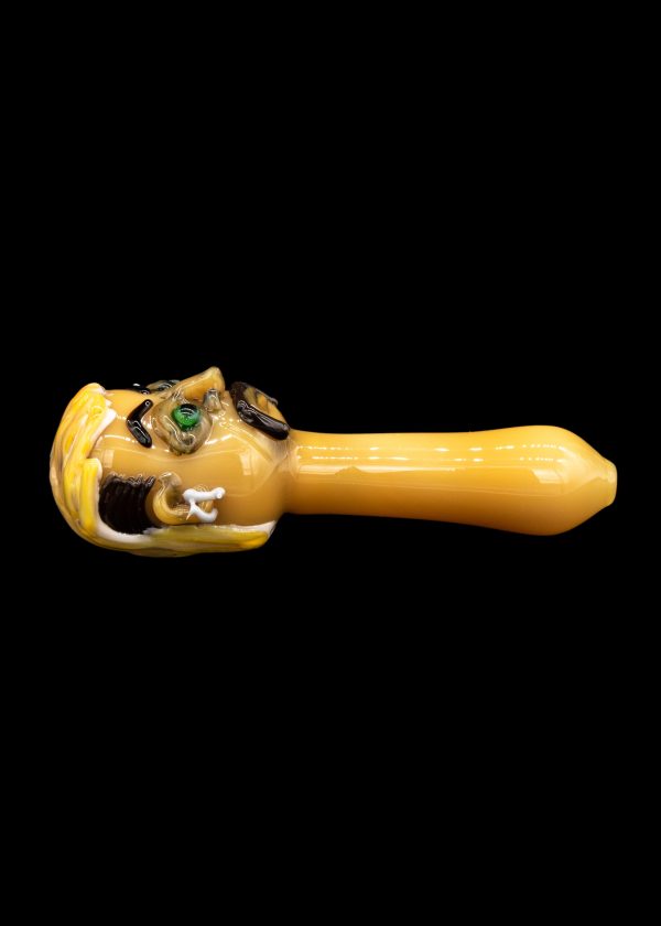 Hand-blown glass pipe shaped like a cartoon monster's head, with green eyes and an open mouth, on a black background.