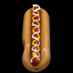 Glass hot dog-shaped cannabis pipe with red, yellow, and white accents, isolated on black.