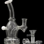 Clear glass bubbler water pipe with accompanying bowl and accessories, reflecting on a dark surface.