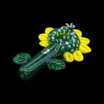 Hand-blown glass pipe shaped like a sunflower, with green and yellow hues, against a black background.