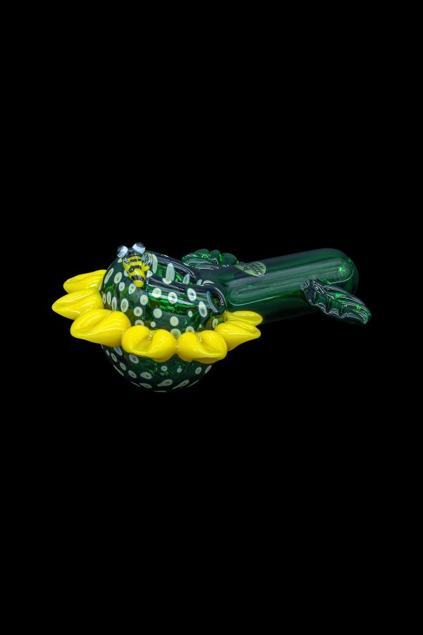 Hand-blown glass cannabis pipe shaped like a bee resting on a yellow flower.