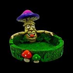 Ceramic ashtray shaped like a smiling mushroom man with smaller mushroom and leaf details, isolated on a black background.