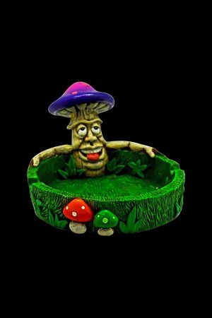 Ceramic ashtray shaped like a smiling mushroom man with smaller mushroom and leaf details, isolated on a black background.