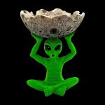 Green alien sculpture holding a speckled stone ashtray or catch-all, isolated on black.