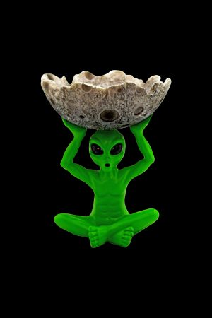 Green alien sculpture holding a speckled stone ashtray or catch-all, isolated on black.