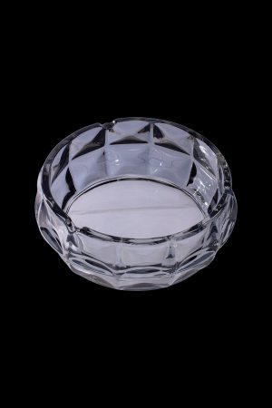 Clear glass ashtray with a geometric faceted design, isolated on a black background.