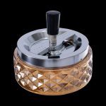 A metallic and glass grinder for cannabis, featuring a faceted amber-colored base and a silver grinding mechanism with a black knob.