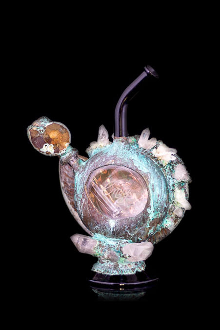 Hand-blown glass water pipe with a unique, organic shape, featuring copper-colored accents and crystalline formations, set against a black background.