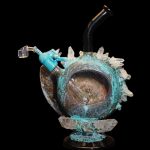 A detailed glass water pipe shaped like a pumpkin, adorned with crystal-like spikes and a turquoise-blue glaze, set against a black background.