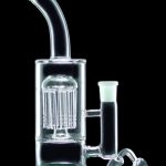 Clear glass water pipe (rig) with a perc diffuser and accompanying glass bowl, isolated on black.