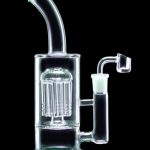 Glass water pipe with intricate percolator and quartz nail, illuminated with green light.