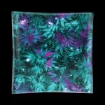 A vibrant glass ashtray with a galaxy-inspired design featuring cannabis leaves and sparkling accents, against a black background.