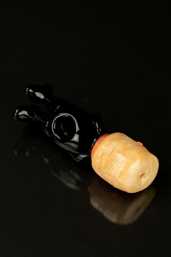 Glossy black glass pipe resembling a hand, with a peach-colored mouthpiece, isolated on a black reflective surface.