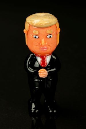 A glossy, cartoonish figurine of Donald Trump in a suit, likely a novelty item related to cannabis accessories.