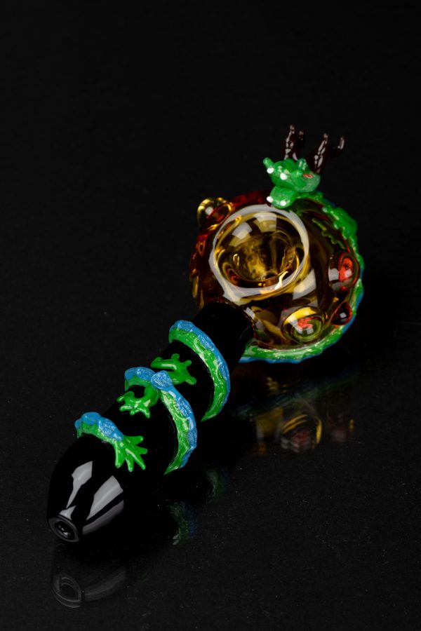 Hand-blown glass pipe with a vibrant green lizard design and intricate detailing, displayed on a reflective black surface.