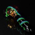 Intricately designed glass cannabis pipe with a vibrant green and blue pattern, displayed against a black reflective surface.