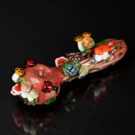 Hand-blown glass pipe decorated with colorful mushroom designs, reflecting on a dark surface.