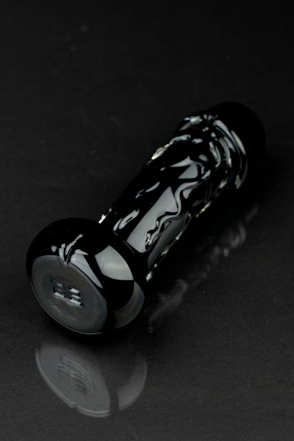 Black glass pipe with intricate white swirls, resting on a reflective surface.