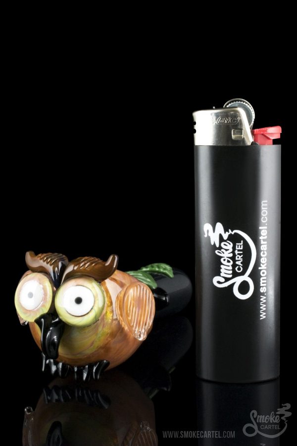 A colorful glass owl figurine sits beside a black lighter branded with ""Smoke Cartel"" and its website address."