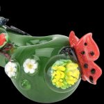 A side view of the Empire Glassworks Spoon Pipe - Garden Critters, featuring sculpted flowers and insects on green glass.