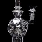 Clear glass water pipe (bubbler) with intricate skull design, isolated on black.