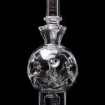 Clear glass water pipe with sculpted skull inside spherical chamber, studio shot.