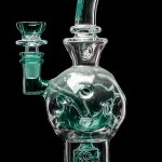 A clear glass water pipe (bong) with green accents and sculpted details, isolated on a black background.