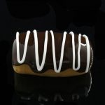 A close-up shot of the Glassheads "Sweet Eclair" Chillum on a dark surface, highlighting its smooth, curved glass design.