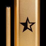 Gold-toned cannabis smoking tube with a black star logo and accompanying metal pick.