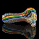 A side view of the Heavy Cane Worked Rainbow Spoon - Rainbow Mega Pipe shows colorful glasswork reflected on a dark surface.
