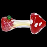 Red glass mushroom pipe with white spots and a green leaf detail, isolated on a black background.