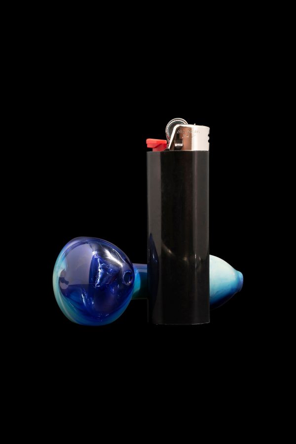 Glass cannabis smoking piece and black lighter isolated on black background.