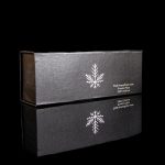 Black box with a snowflake design and cannabis accessory branding, reflected on a dark surface.