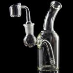 Clear glass dab rig with quartz banger, reflecting on a dark surface.