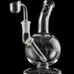 Clear glass dab rig with intricate design and accompanying nail, isolated on a black background.