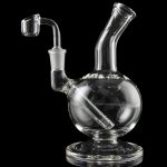 Clear glass dab rig with a quartz nail, reflecting on a black surface.