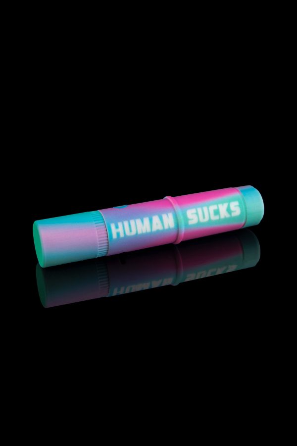 A colorful, cylindrical smoking kit with the text "HUMAN SUCKS" printed on its side, reflected on a black surface.