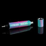 Iridescent cannabis oil syringe and accompanying mouthpiece reflected on a black surface, text reads "HUMAN SUCKS."