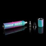 A disassembled cannabis oil vape pen with a colorful, gradient finish and the phrase “HUMAN SUCKS” printed on its side, displayed on a reflective surface against a black background.